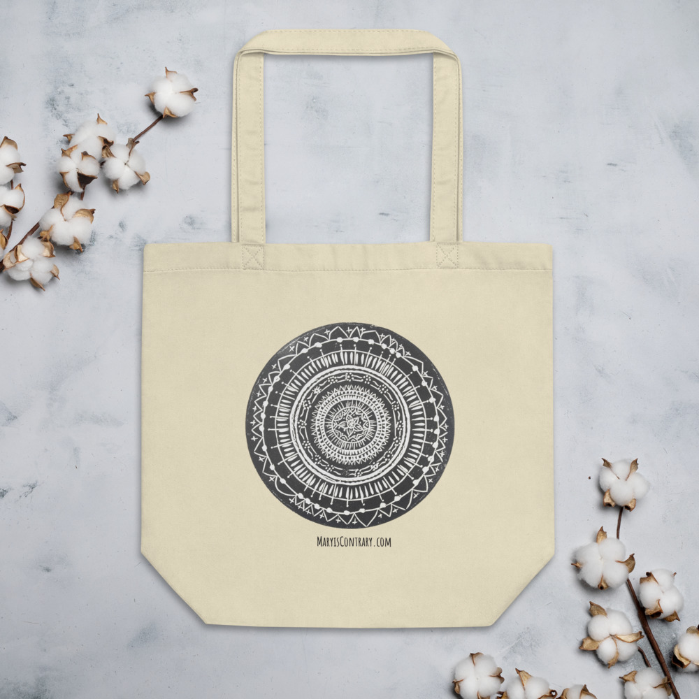 This is an image of a tote bag with a black and white mandala printed in the front. The bag is made from organic cotton